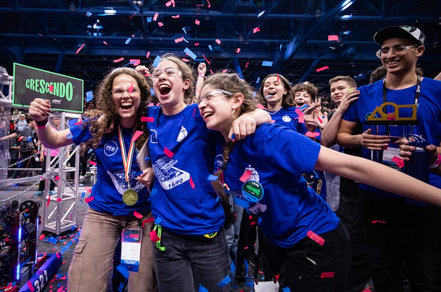 Students celebrate while holding a FIRST trophy while confetti falls during the 2024 FIRST Championship.